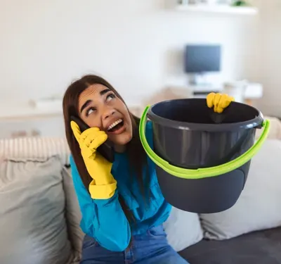 Woman holding bucket under leaking roof.