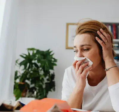 Woman sneezes into tissue at home, struggling with allergies and mold.